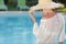 Woman in a dress and sunhat sits next a resort pool