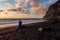 Woman in dress walking barefoot on volcanic sand beach Playa del Ingles during sunset in Valle Gran Rey on La Gomera,