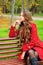 Woman dressed in red coat sitting in autumn park.