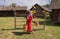 A woman dressed in Russian folk costume, standing with a yoke at the rustic fence.