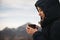 Woman dressed warmly stands with a mug of hot drink in her hands against the background of the mountains