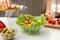 Woman dressing fresh vegetable salad with olive oil in kitchen