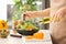 Woman dressing fresh vegetable salad with olive oil in kitchen