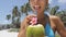 Woman drinking fresh coconut water with straw on Caribbean beach