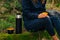 Woman drinking tea from thermos during hike outdoors. Refreshment during hiking in the woods