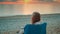 Woman drinking from thermal mug and sitting on the beach before sunrise