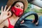 Woman driver sitting in car wearing protective mask during coronavirus pandemic. Girl shows ok cool sign