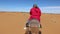 A woman on a dromedary in a pink tunic and turban walking through the Erg Chebby desert of Morocco