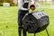 A woman is dumping a small bin of kitchen scraps into an outdoor tumbling composter in backyard garden