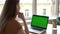 Woman with earphones looks at laptop with chromakey screen