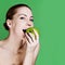 Woman eating apple smiling on green background.