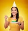 Woman is eating birthday cake, celebration and happy in portrait, rainbow dessert and candle on yellow background