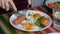 Woman eating breakfast. Knife and fork in hand. American style breakfast with fried eggs, sausage, salad and toast.