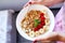 Woman eating healthy breakfast bowl, hold in hand granola, seeds, fresh strawberry, banana, top view, copy space.