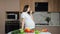 Woman eats vegetables stroking pregnant belly in kitchen