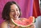 A woman eats a watermelon and laughs