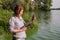 Woman ecologist on river bank examines sample of green algae and holds tablet