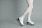 Woman in elegant white ice skates on grey background, closeup of legs. Space for text