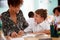 Woman Elementary School Teacher Giving Male Pupil Wearing Uniform One To One Support In Classroom