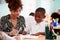 Woman Elementary School Teacher Giving Male Pupil Wearing Uniform One To One Support In Classroom