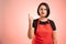 Woman employed at supermarket with red apron and black t-shirt counting one with her finger