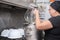 Woman employee loading casseroles into an industrial dishwasher in the restaurant.