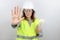 Woman engineer with hardhat and reflecting jacket with open hand doing stop sign with serious and confident expression