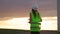 Woman engineer in uniform and helmet holding joystick controlling flying drone working at windmill. Alternative electrical energy