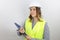 Woman engineer wearing hardhat and reflecting jacket lookng away, holding flip board.