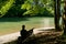 Woman enjoys sitting on a bench under shady trees on an idyllic river bank