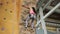 Woman in equipment hardly climbs up artificial rock wall.