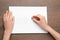 Woman erasing word on sheet of white paper at wooden table, top view