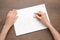 Woman erasing word on sheet of white paper at wooden table, top view