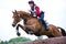 Woman eventer on horse jumping over Log fence