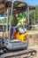 Woman excavator on a small excavator with yellow warning vest wearing the sanitary protective mask that makes the gesture of every