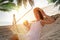 Woman with exotic cocktain relaxing in hammock under green palm leaves on sunlit beach