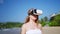 Woman explores virtual world on tropical beach in VR headset, sways to immersive experience in sunny setting. Natural