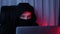 Woman face in black mask and hoodie looking at computer screen and breaking password. Young hacker breaks security protection on l