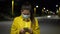 Woman in face mask looks smartphone. Young female in night city, wears protective medical face mask in fear of
