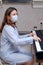 A woman in a face mask plays a home digital piano, problems with learning music during a period of isolation in quarantine