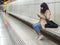 Woman with face mask sitting in a subway station looking and playing with cellphone.