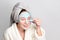 Woman with facial clay mask at spa salon or at home, skincare theme. Girl removes alginate cosmetic mask. Face mask, spa
