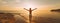 Woman facing the sunset with her hands up standing on a sea beach