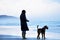 Woman and faithful friend dog alone on stunning beach watching ocean