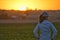 Woman farmer standing on field looking distance in sunset