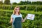 Woman farmer working in a strawberry field. Biologist inspector examines strawberry bushes and shows the level of crop growth usin