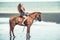 Woman fashion model riding a horse on the beach.