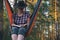 Woman in fedora hat reading book while sitting in hammock in pine forest at sunset. Mindfulness, relax on nature, treat yourself,