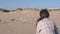 Woman is feeding birds gulls and crows on a sandy beach with dunes.