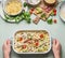 Woman female hands holding pasta casserole with romanesco cabbage and ham in creamy sauce, on kitchen table background with ingred